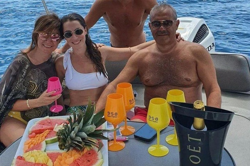 A group of people on a boat with a table set with drinks and fruit. 3