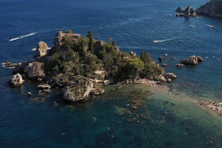 Eine felsige Insel mit klarem, blauem Wasser, umgeben von kleineren Felsen und einigen Gebäuden. 5