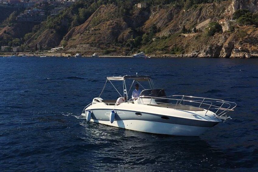 A white motorboat on calm water with a rocky coastline in the background. 2