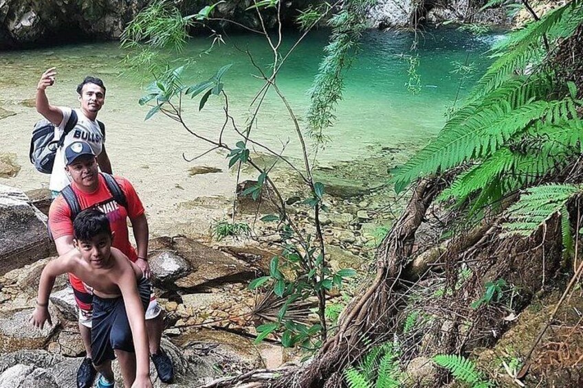 Trois personnes se trouvent près d’une étendue d’eau claire, bordée de rochers et de végétation. 3