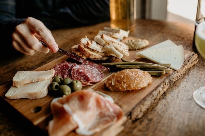 A wooden board with various cheeses, cured meats, olives, and bread. 1