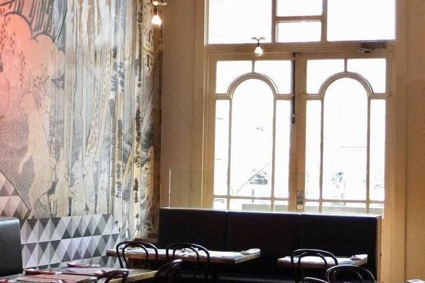 A restaurant interior with a large window, patterned wallpaper, and a seating area. 5