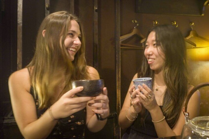 Twee personen houden kleine voorwerpen vast, mogelijk bekers, in een donkere ruimte. 1