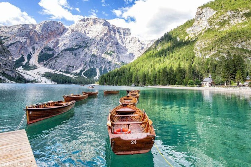 Ein See mit hölzernen Booten, einem Holzsteg und Bergen im Hintergrund. 2