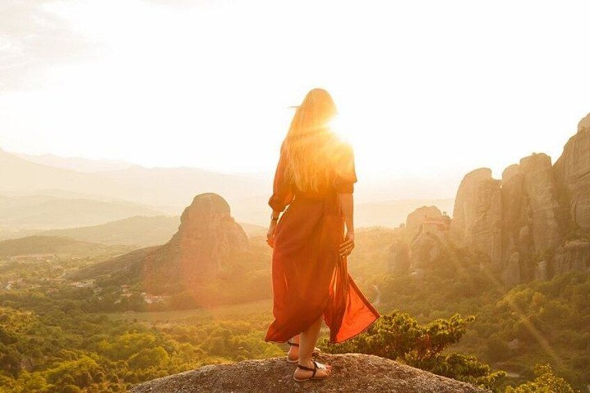 A person in a red dress standing on a rock with a mountainous landscape in the background. 1