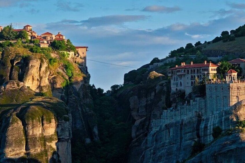 A cliffside with buildings perched on top, a narrow passage between rock formations, and a clear sky. 2