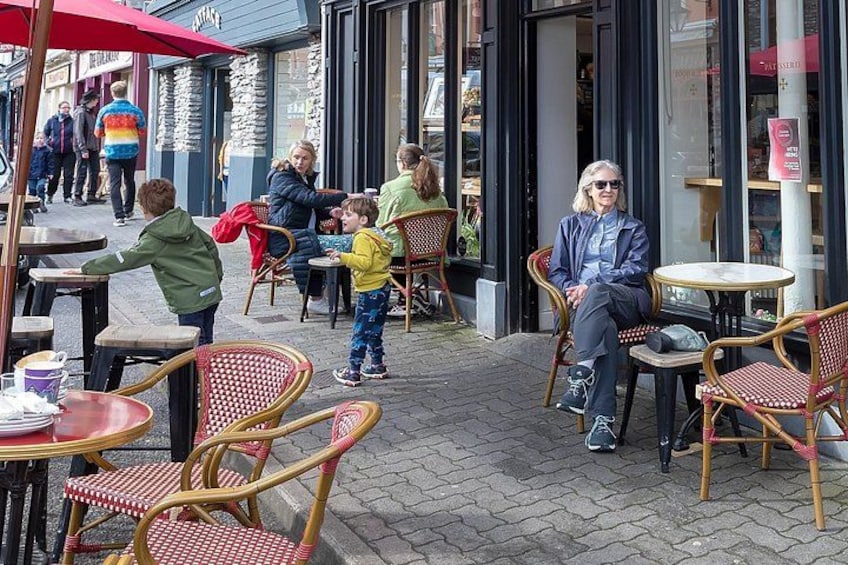 Outdoor cafe seating with wicker chairs and tables, a person sitting at a table, and another person walking by. 2
