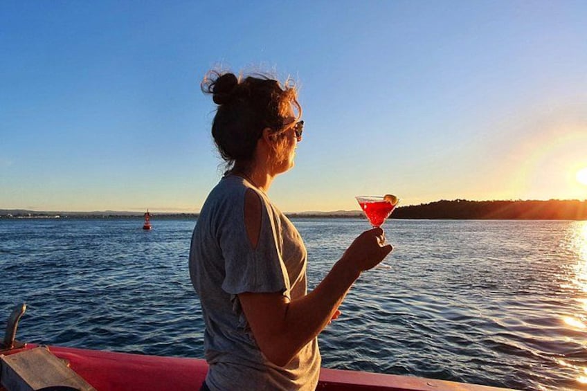 A person holding a drink on a boat with a sunset in the background. 2