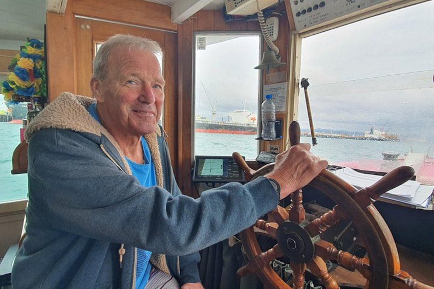 A person steering a ship's wheel, with a view of the sea and other ships in the background. 3