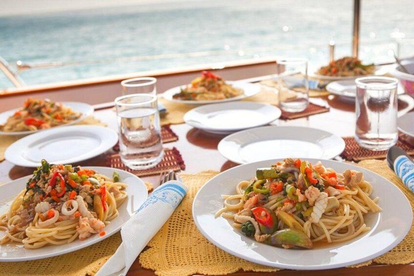 A table set for a meal with plates of pasta and glasses of water, overlooking the sea. 1