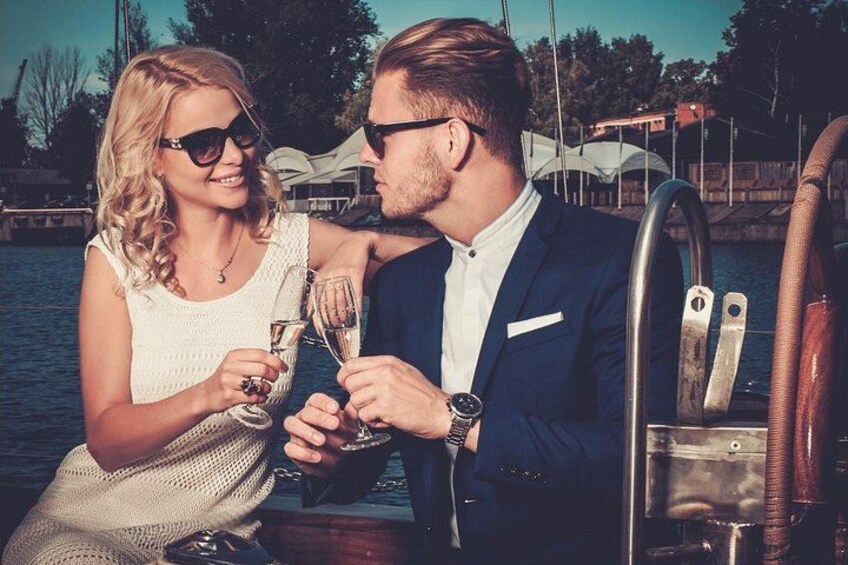 Two people toasting with champagne glasses on a boat, with water and docked boats in the background. 4