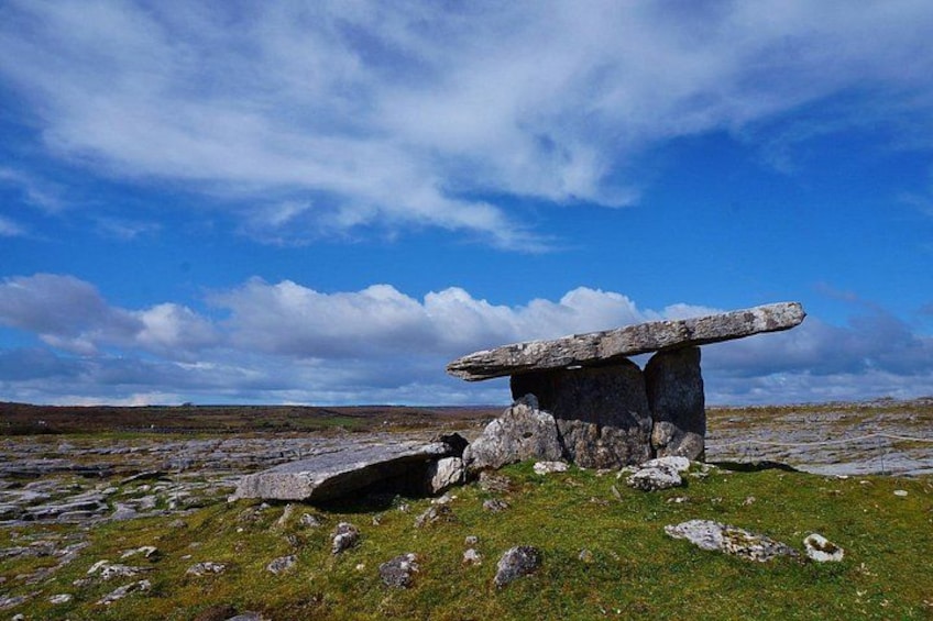 A stone structure with a flat top, surrounded by grass and rocks, under a partly cloudy sky. 2
