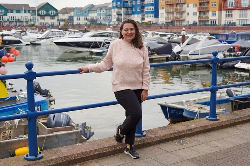 A person standing by a waterfront with boats and colorful buildings in the background. 2