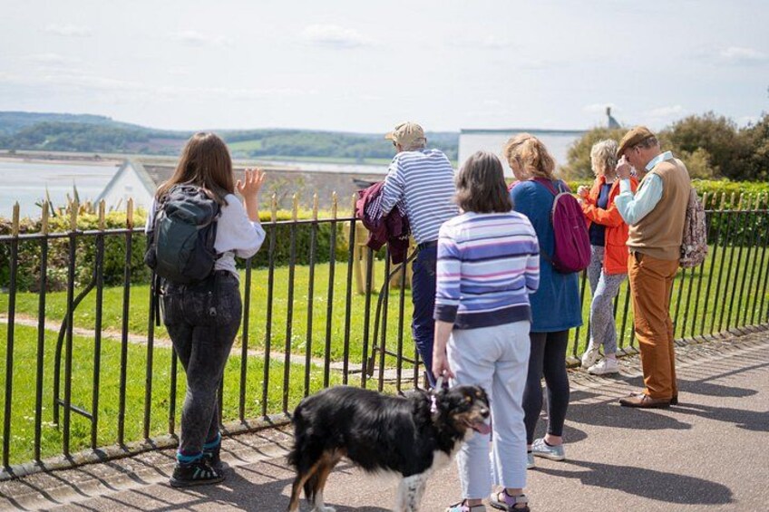 A group of people standing by a fence overlooking a body of water, with a dog in the foreground. 1