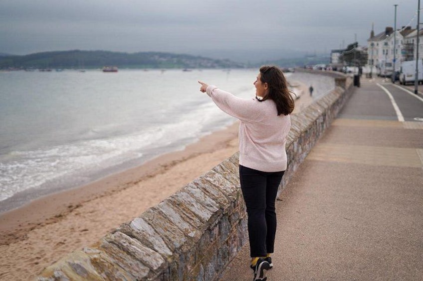 A person standing on a stone wall overlooking a beach with a road and buildings in the background. 4