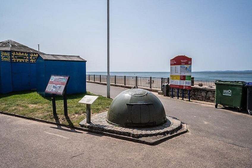 A coastal road with a blue building, a spherical structure, a signboard, and a trash bin. 3
