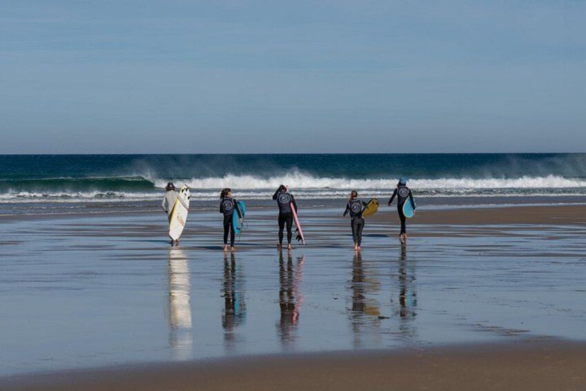 A beach with surfers walking towards the water, holding surfboards. 2