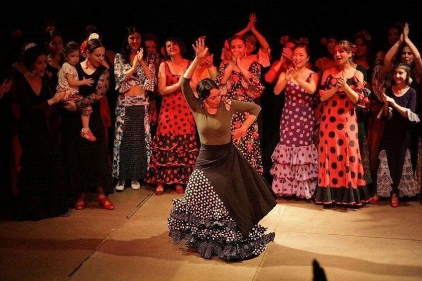 A dance performance with a woman in a polka dot dress and a crowd clapping. 1