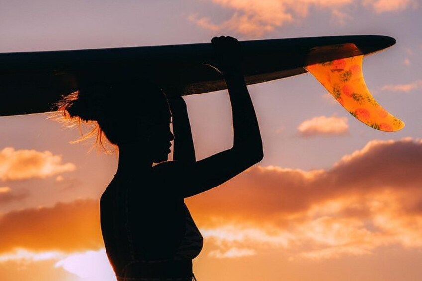 A person carrying a surfboard against a sunset sky. 2
