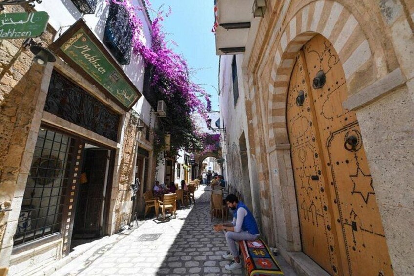Une rue étroite pavée de pierres, une femme assise sur un banc et une boutique dont l’enseigne est écrite dans une langue étrangère. 5
