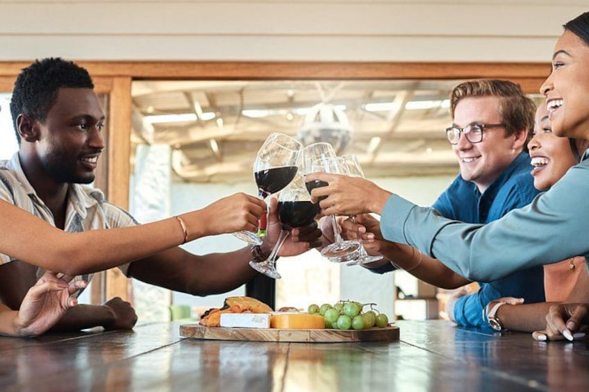 A group of people toasting with wine glasses at a wooden table with a fruit platter. 4