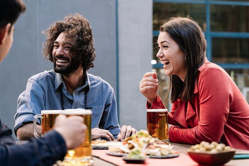 Three people sitting at a table with food and drinks. 1