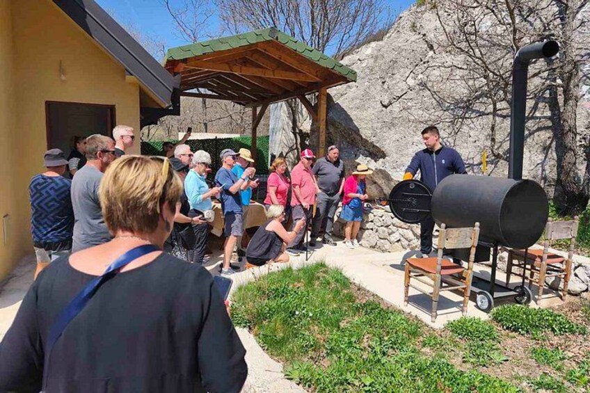 Un grupo de personas reunidas alrededor de una parrilla al aire libre, con un edificio y montañas al fondo. 3