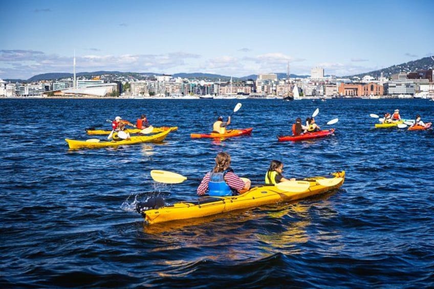 Personas haciendo kayak en un cuerpo de agua con un paisaje urbano al fondo. 4