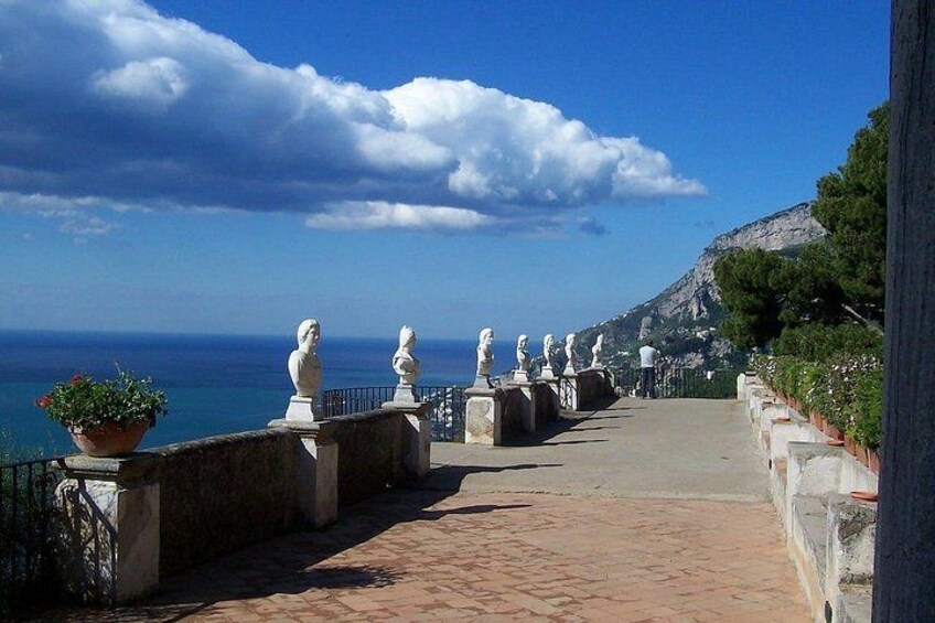 A coastal walkway with statues, a clear sky, and the sea in the background. 2