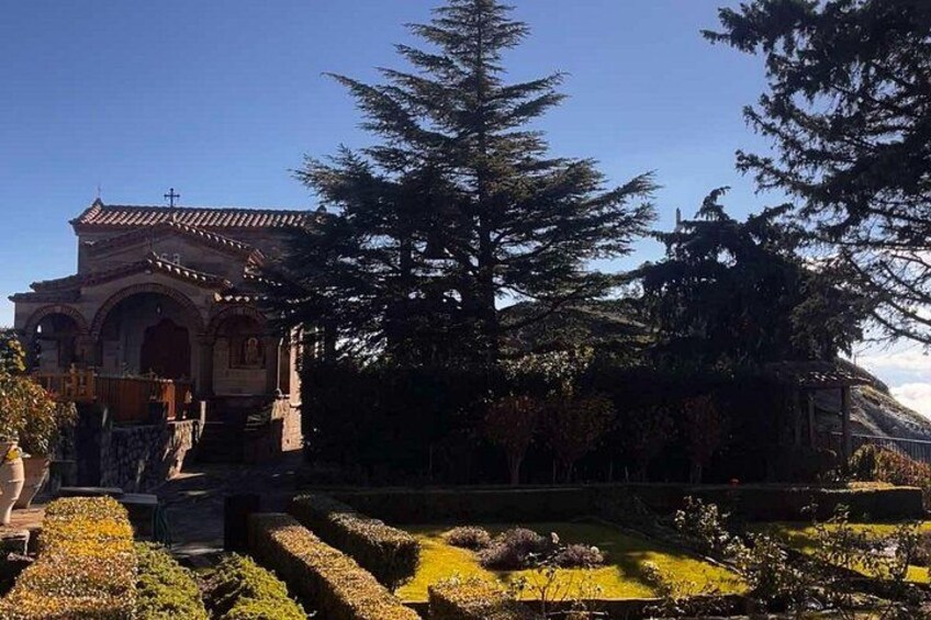 A church with a tiled roof, surrounded by a well-maintained garden with trimmed hedges and a large evergreen tree. 5