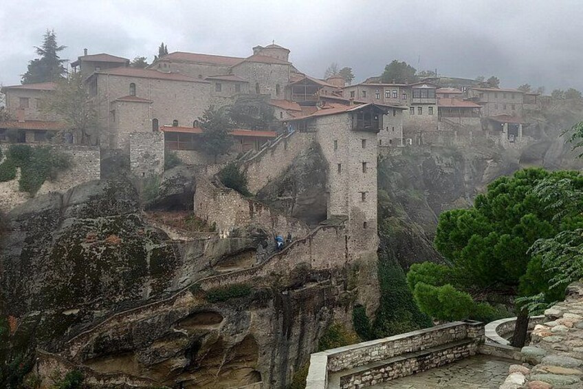 A historic stone fortress with multiple buildings perched on a cliff, surrounded by rocky terrain and greenery. 2
