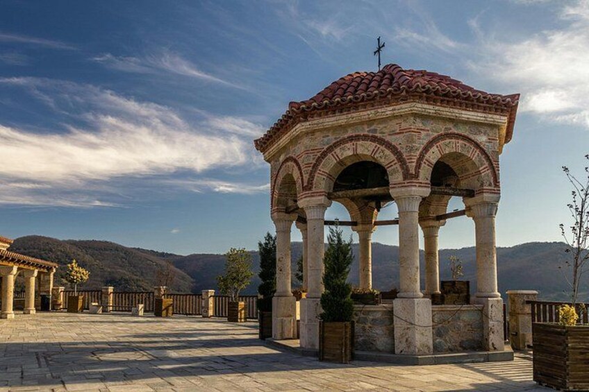 A historical stone pavilion with arches, surrounded by a paved area and a mountainous backdrop. 3