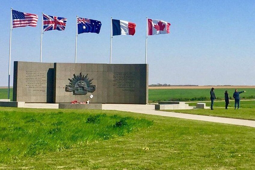 A memorial with flags of the USA, UK, Australia, and Canada, and two people standing by it. 1