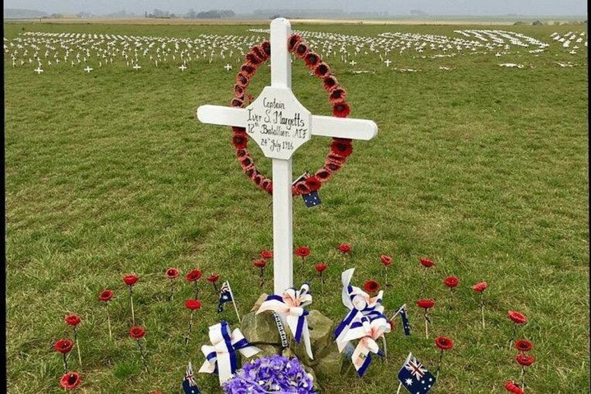 A memorial cross with a wreath, surrounded by red poppies and flags. 2