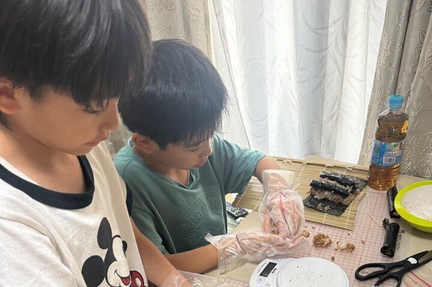 Two individuals preparing food, with sushi on a bamboo mat and a bottle of sauce on the table. 4