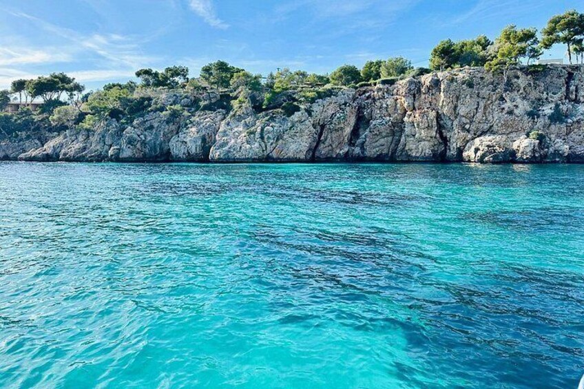 A coastal landscape with clear turquoise waters, rocky cliffs, and trees. 2