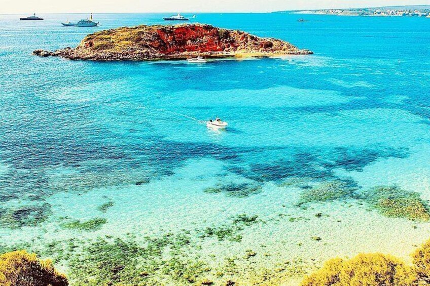 A coastal scene with clear turquoise waters, a small rocky island, and several boats. 5