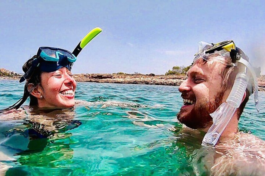 Due persone fanno snorkeling in acque cristalline blu con scogliere rocciose sullo sfondo. 3