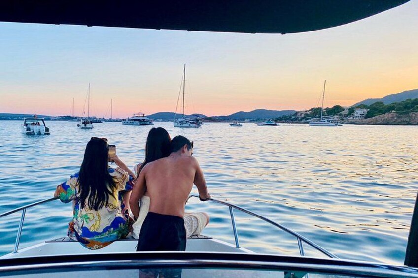 Un bote con tres personas en el agua, rodeado de otros botes y un atardecer de fondo. 4
