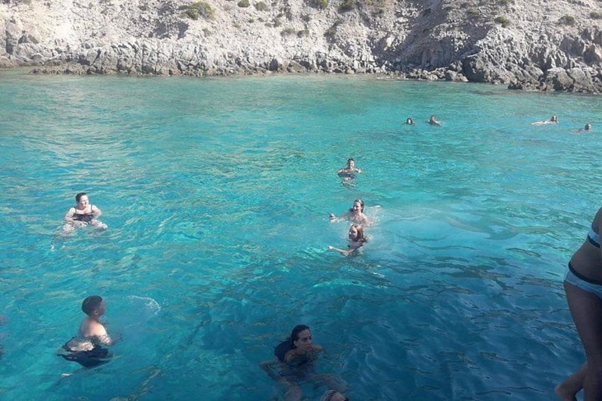 Personas nadando en aguas azul cristalina, con acantilados rocosos al fondo. 5