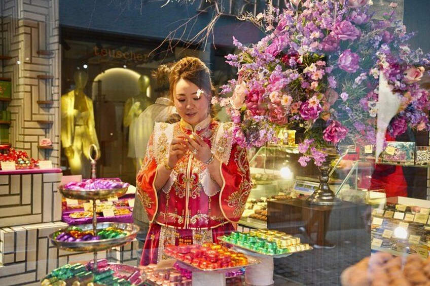 A person in traditional attire at a market stall with colorful sweets and flowers. 4