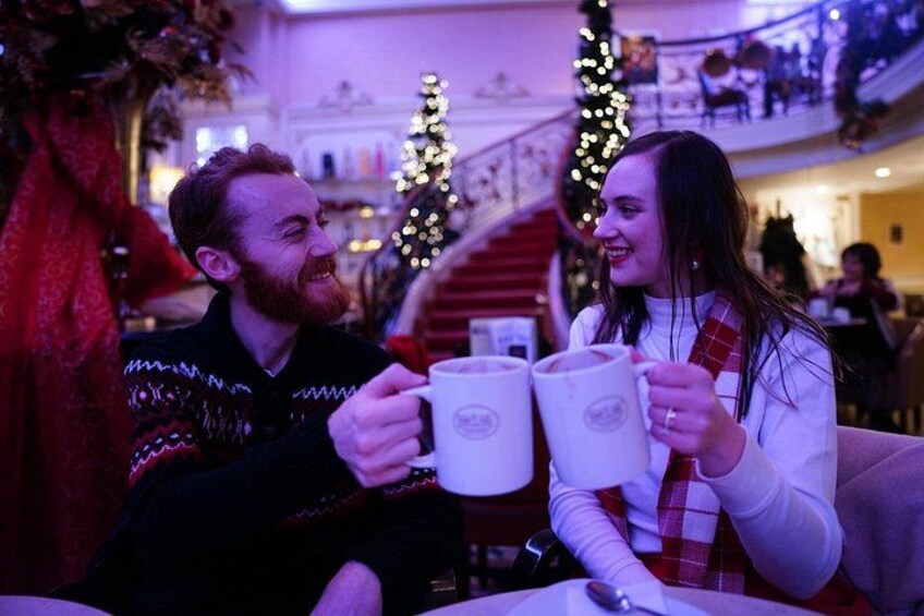 Two people holding mugs, a Christmas tree, and a staircase in a decorated indoor setting. 3