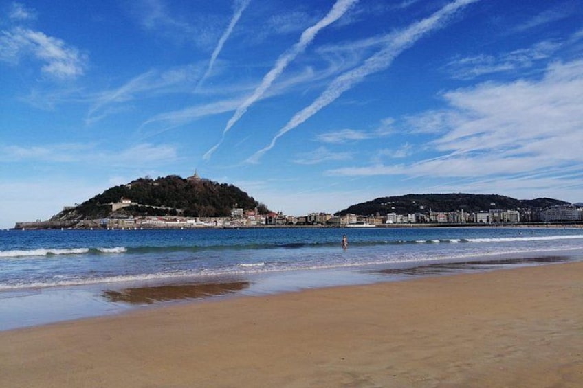 Ein Strand mit einer Hügelkulisse, blauem Himmel und einigen Gebäuden am Wasser. 5