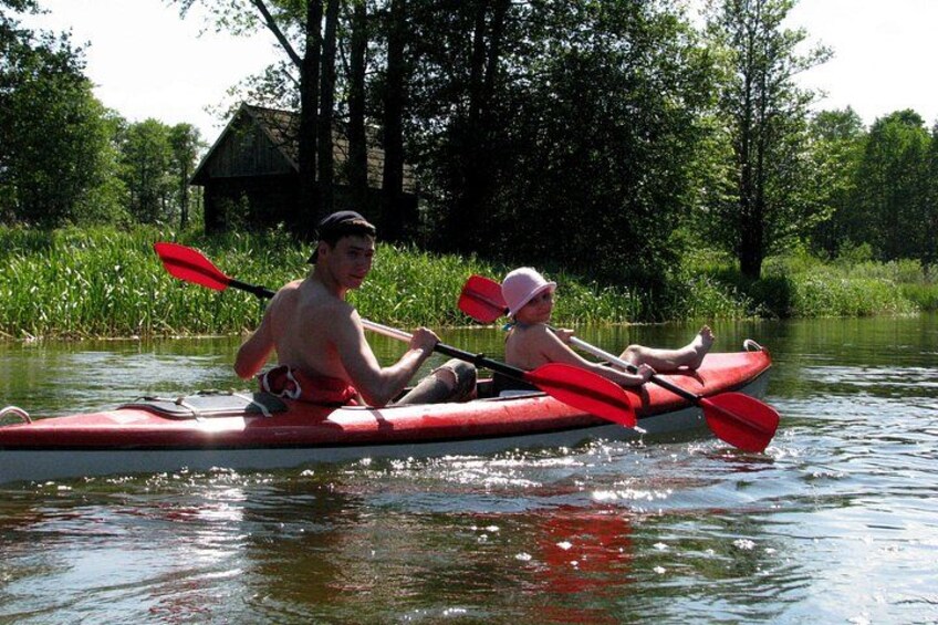 Two people kayaking on a calm river surrounded by greenery. 1