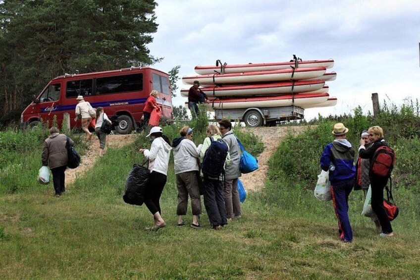 A group of people walking towards a red van and a trailer with white canoes. 2