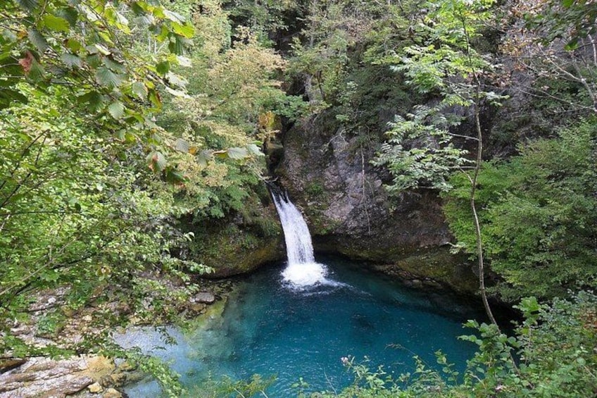 A waterfall in a forested area with clear blue water. 1