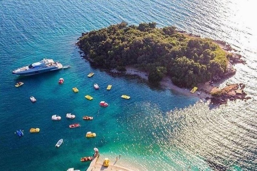 An aerial view of a small island with clear turquoise waters, surrounded by boats and a yacht. 2