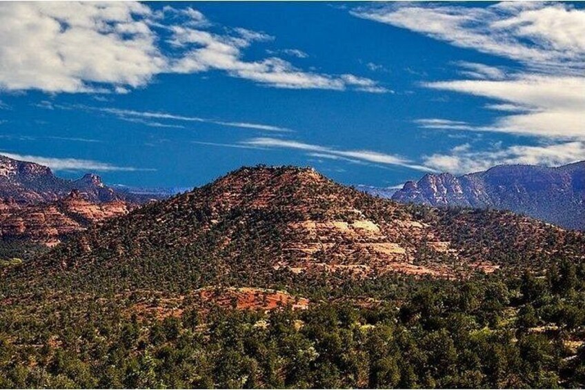 A mountainous landscape with dense forest and rocky terrain under a partly cloudy sky. 3