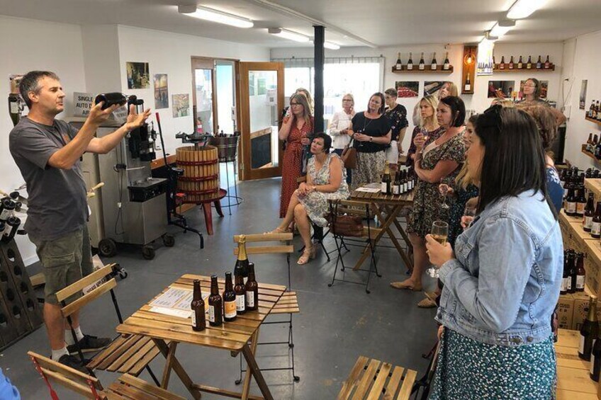 A group of people in a wine tasting room with bottles on tables and a photographer taking pictures. 3