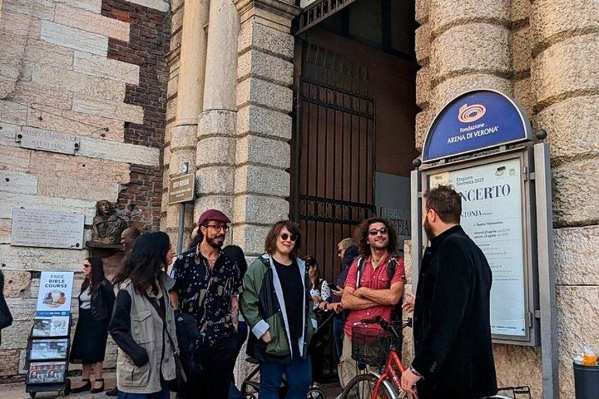 Un gruppo di persone in piedi davanti a un edificio con un cartello che riporta 'Arena di Verona'. 2